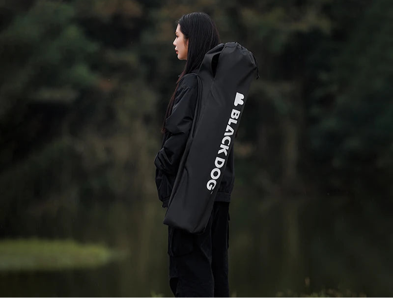 Person wearing a black raincoat with 'Black Dog' branding in a forest setting