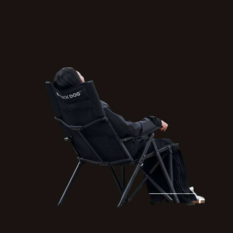 Person sitting on a black camping chair with 'Black Dog' branding in a forest setting.