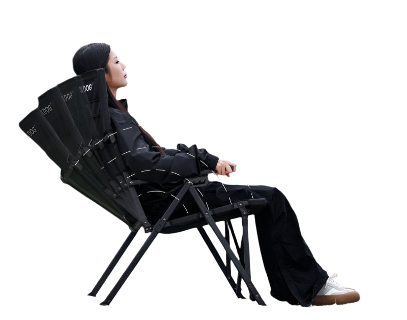Person sitting on a black camping chair with adjustable features, outdoors.