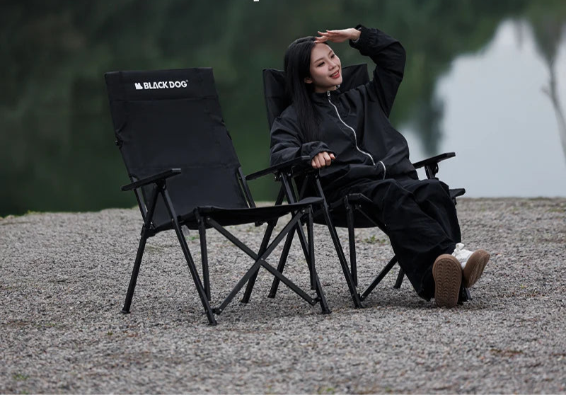 Person sitting on a Black Dog camping chair outdoors with a scenic background