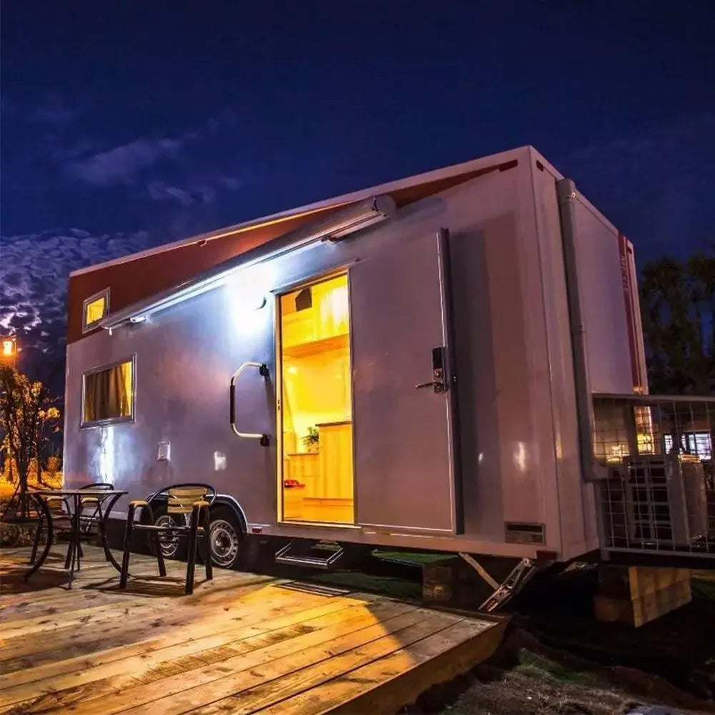 Modern tiny house with open door at night, surrounded by trees and lights.