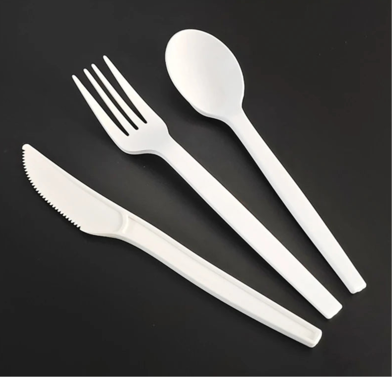 Set of white plastic cutlery including a knife, fork, and spoon on a black background