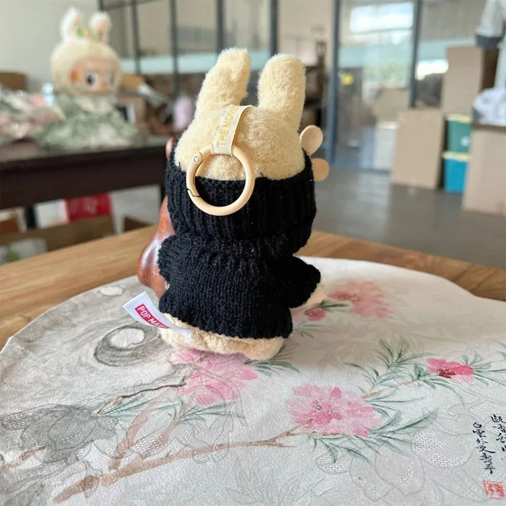 Small plush toy with a black sweater and wooden ring on a floral-patterned surface.