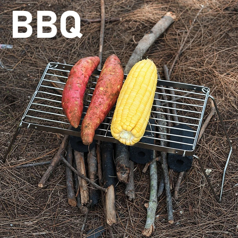 Three sweet potatoes and a corn cob on a metal grill over a bed of sticks and twigs.