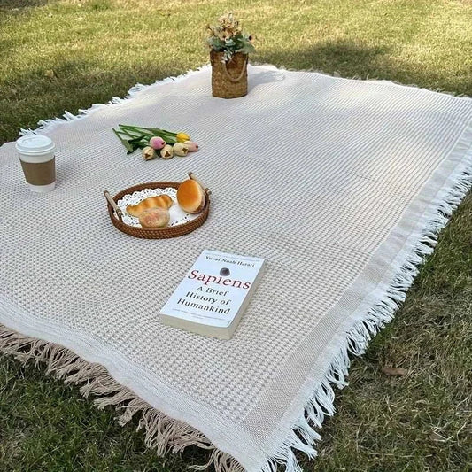 Durable waterproof camping blanket on grass with picnic items.