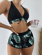 Person wearing a black and green leaf-patterned bikini holding a glass against a white background