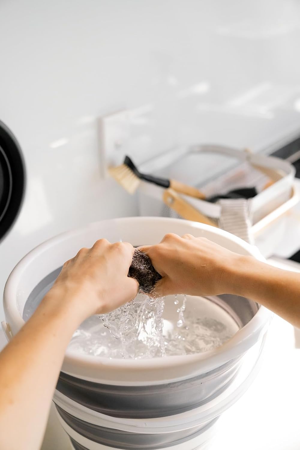 Person washing clothes in a bucket with water and soap.