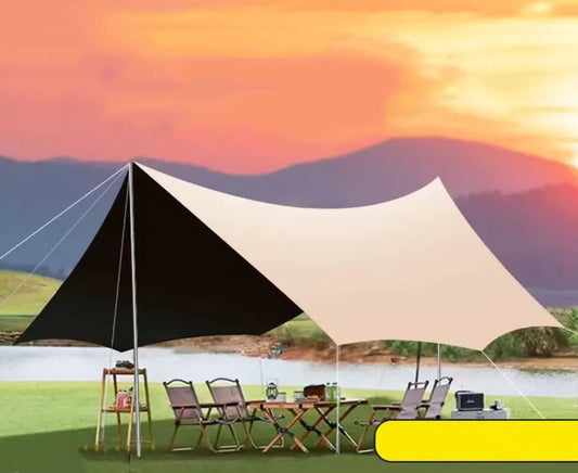 Camping scene with a large canopy, chairs, and a table under a sunset sky.