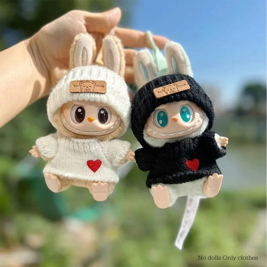 Two plush toys with bunny ears, one in a white outfit with a heart and the other in a black outfit with a heart, held against a blurred natural background.