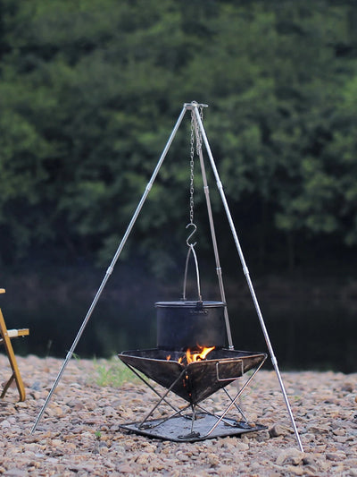 Outdoor cooking setup with a tripod fire pit and hanging pot over a fire.