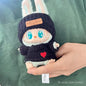 labubu with a black knit hat and sweater held by a hand on a green fabric background.