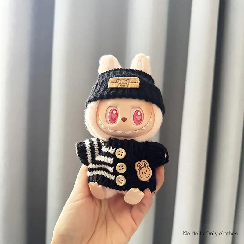 Small plush toy with a black sweater and hat held in a hand against a neutral background