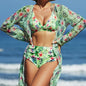 Woman wearing a green floral swimsuit with a matching cover-up on a beach.