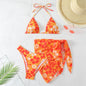 Orange floral bikini set with a straw hat and palm leaves on a light background